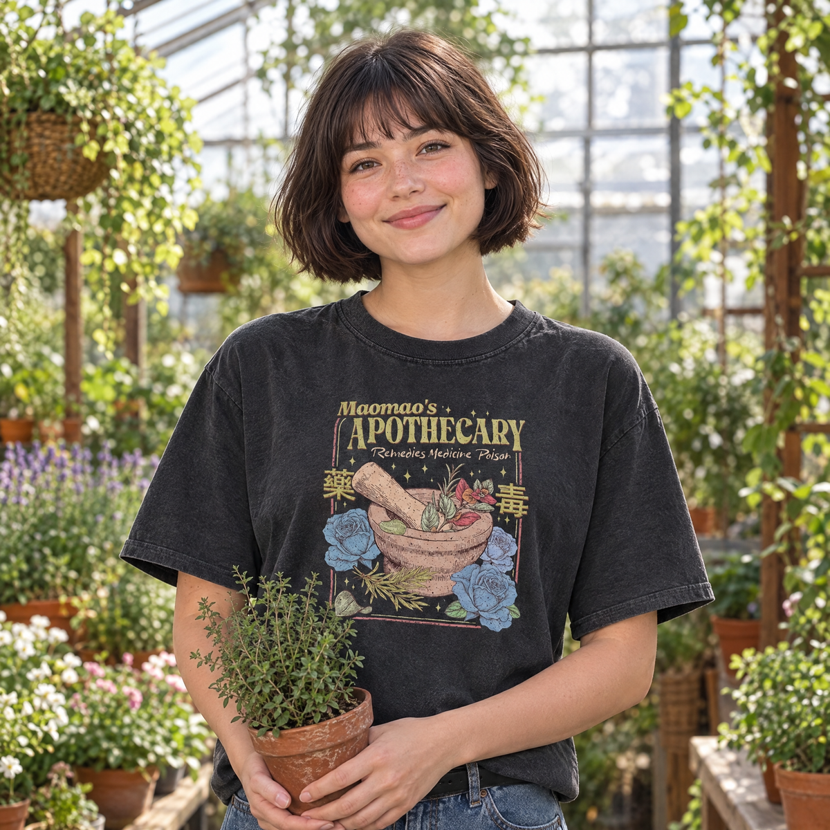 Woman wearing Black Comfort Colors Maomao's Apothecary shirt in a greenhouse holding a potted herb