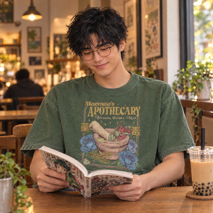 Man wearing Moss Comfort Colors Maomao's Apothecary shirt reading manga in a cafe