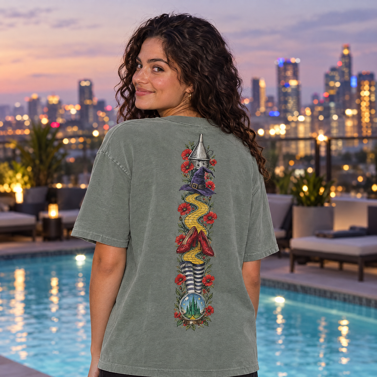 Woman in Sage Comfort Colors Las Vegas shirt showing the back print at a rooftop pool at dusk