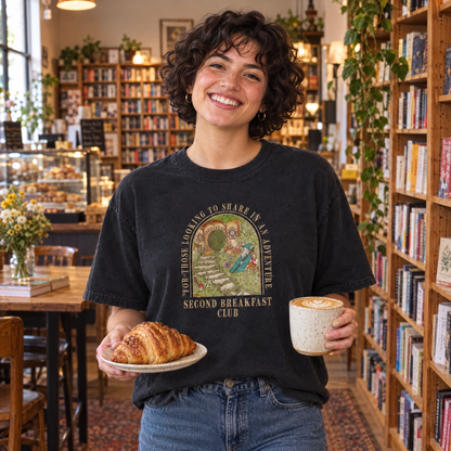 Woman wearing Black Comfort Colors Second Breakfast Club shirt in a bookstore cafe with a croissant