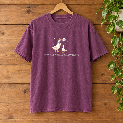 Growing a Silly Little Goose Comfort Colors shirt in Berry on a wooden hanger