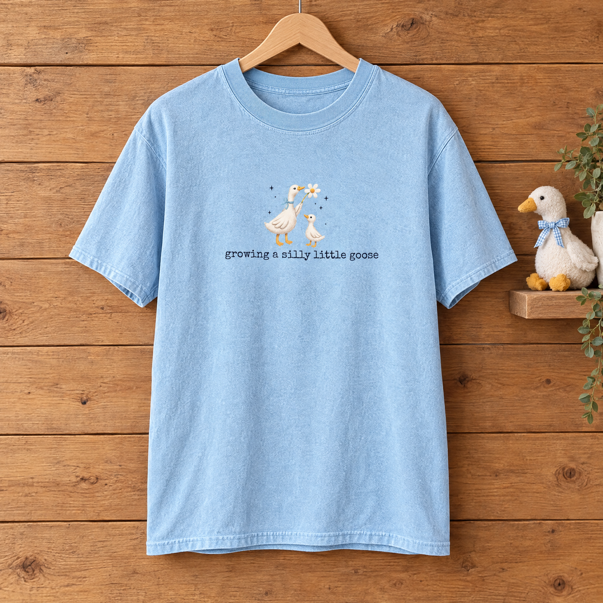 Growing a Silly Little Goose Comfort Colors shirt in Chambray on a wooden hanger