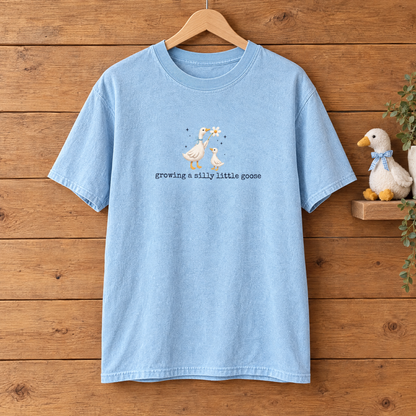 Growing a Silly Little Goose Comfort Colors shirt in Chambray on a wooden hanger