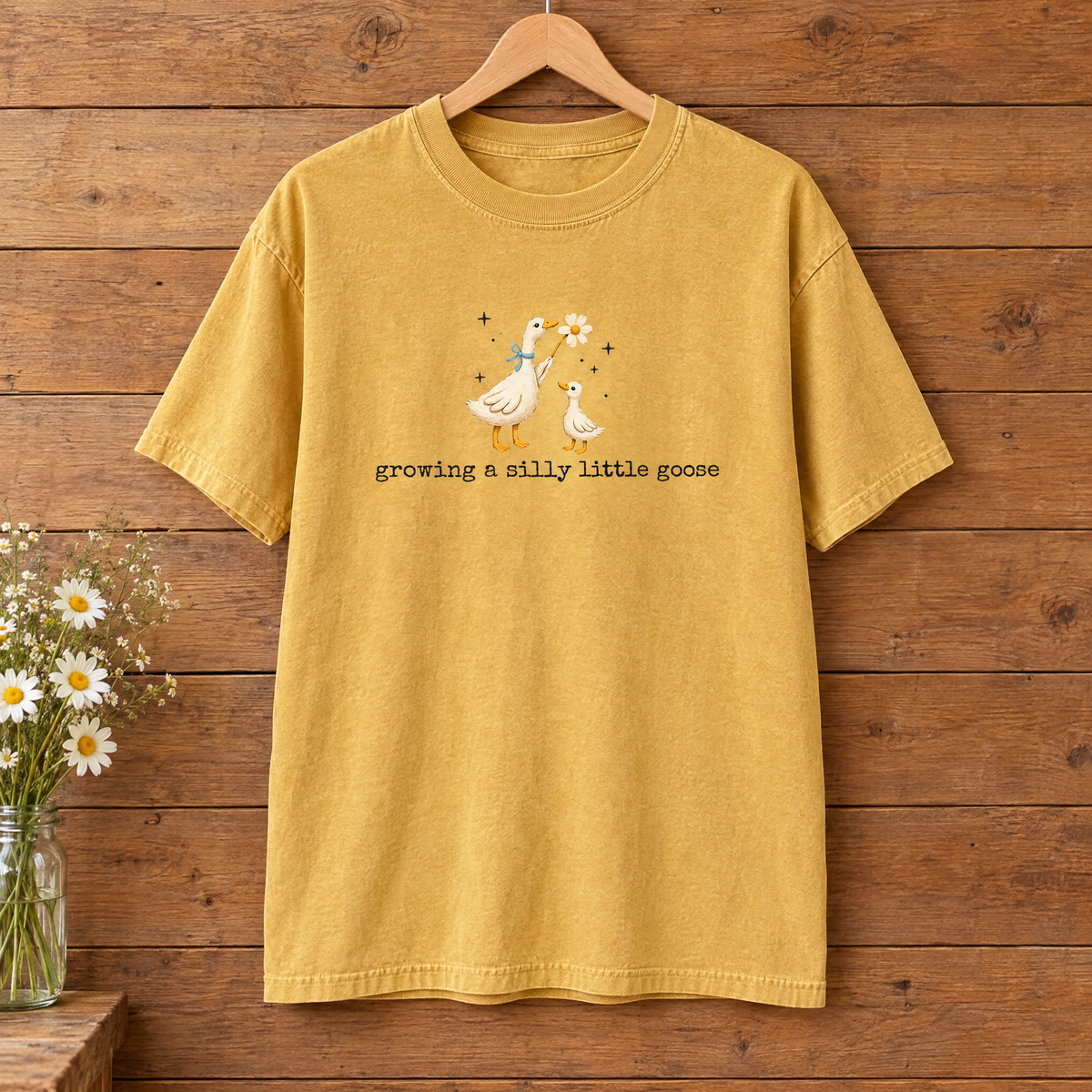 Growing a Silly Little Goose Comfort Colors shirt in Mustard on a wooden hanger