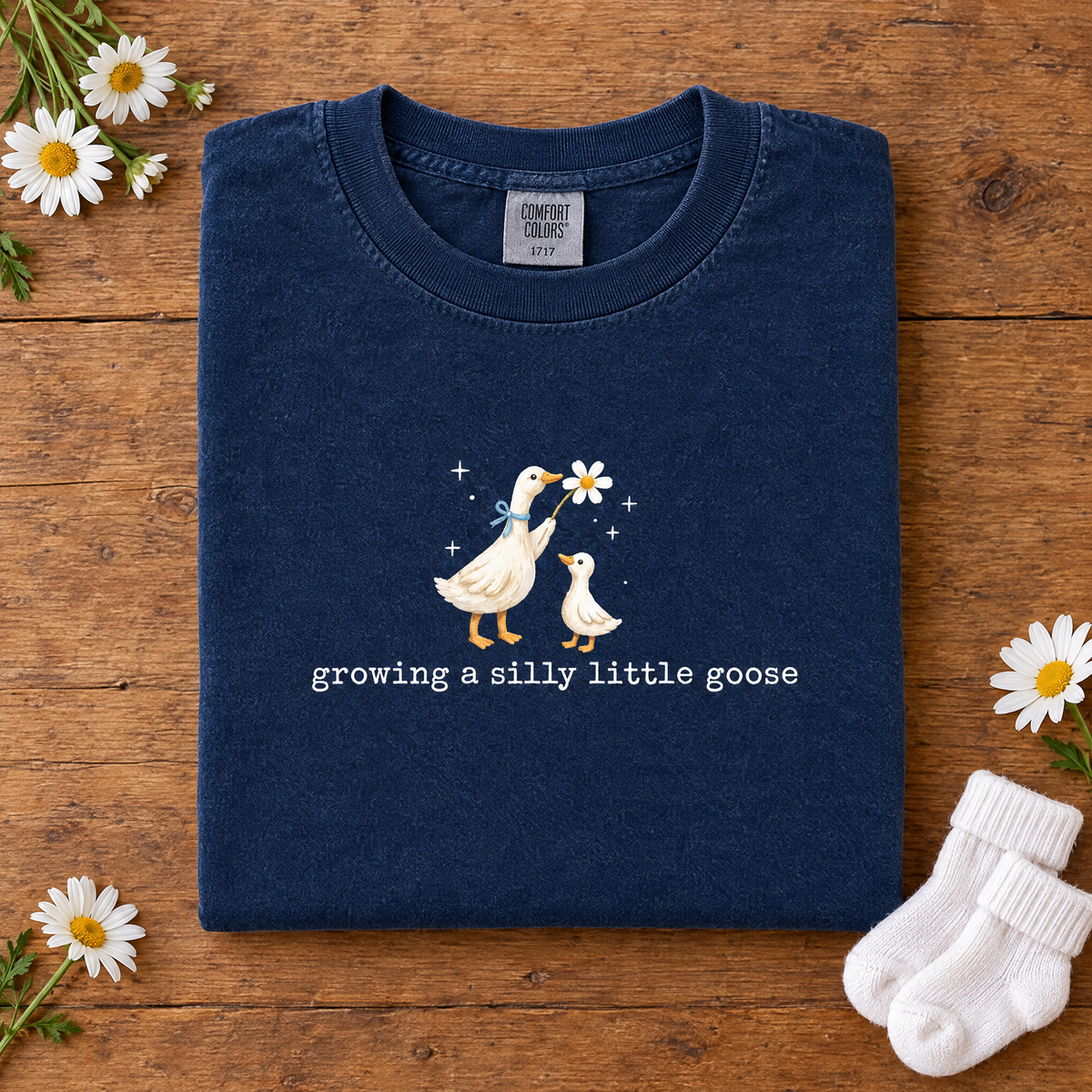 Silly goose pregnancy announcement tee in Navy, folded with baby socks and daisies