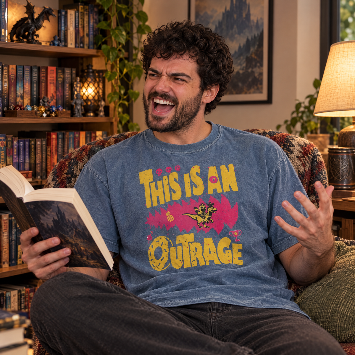 Man wearing Blue Jean Comfort Colors This Is An Outrage shirt with a paperback in a cozy reading nook