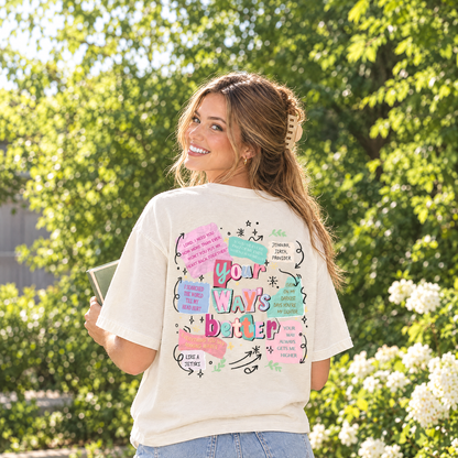 Woman in Ivory Comfort Colors Your Way's Better Christian shirt showing the back collage print in a garden